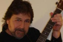 A man holding an acoustic guitar in front of a wall.