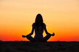 A silhouette of a woman meditating at sunset.