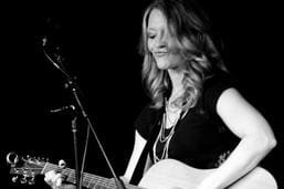 A woman singing and playing an acoustic guitar.