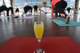 A glass of orange juice in front of a group of people doing yoga.