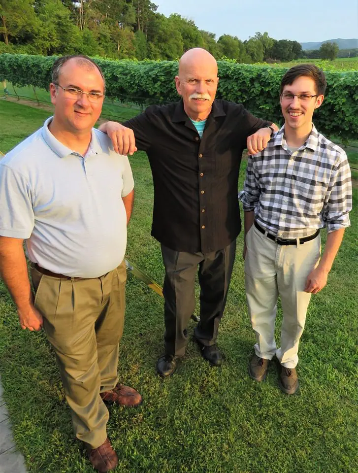 Three men standing in front of a vineyard.