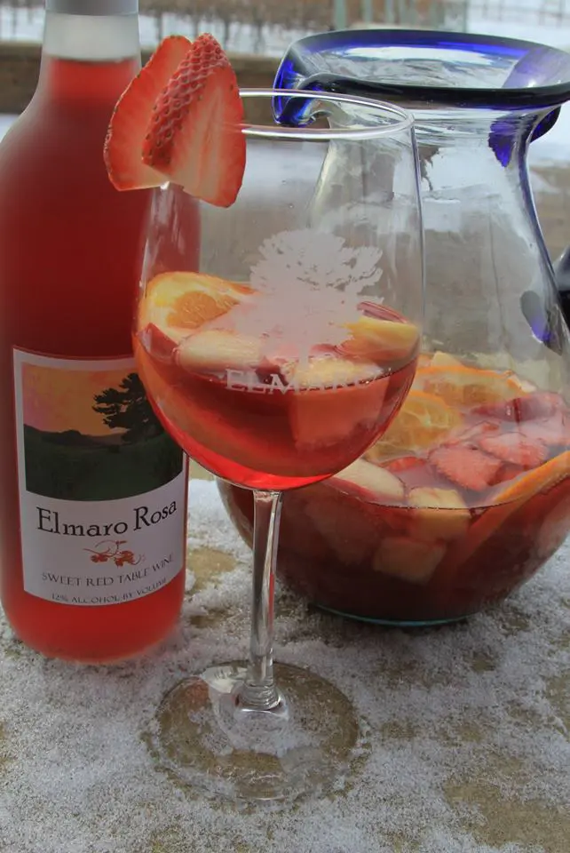 A glass of strawberry sangria next to a bottle of wine.