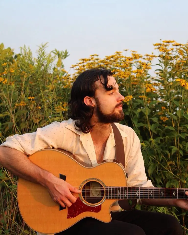 A man sitting in a field with an acoustic guitar.