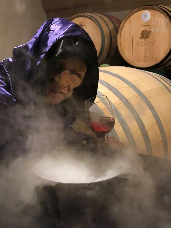 A woman in a black robe is steaming a pot of wine.