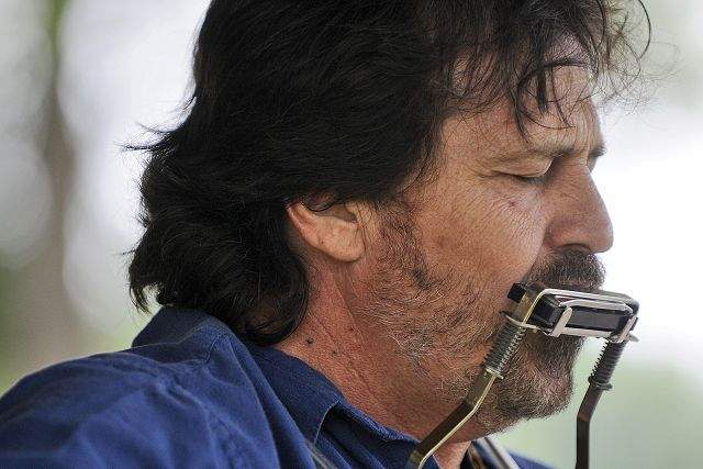 A man with a blue shirt is playing a harmonica.