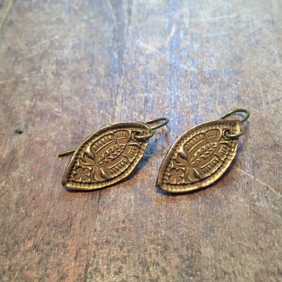 A pair of brass leaf earrings on a wooden table.