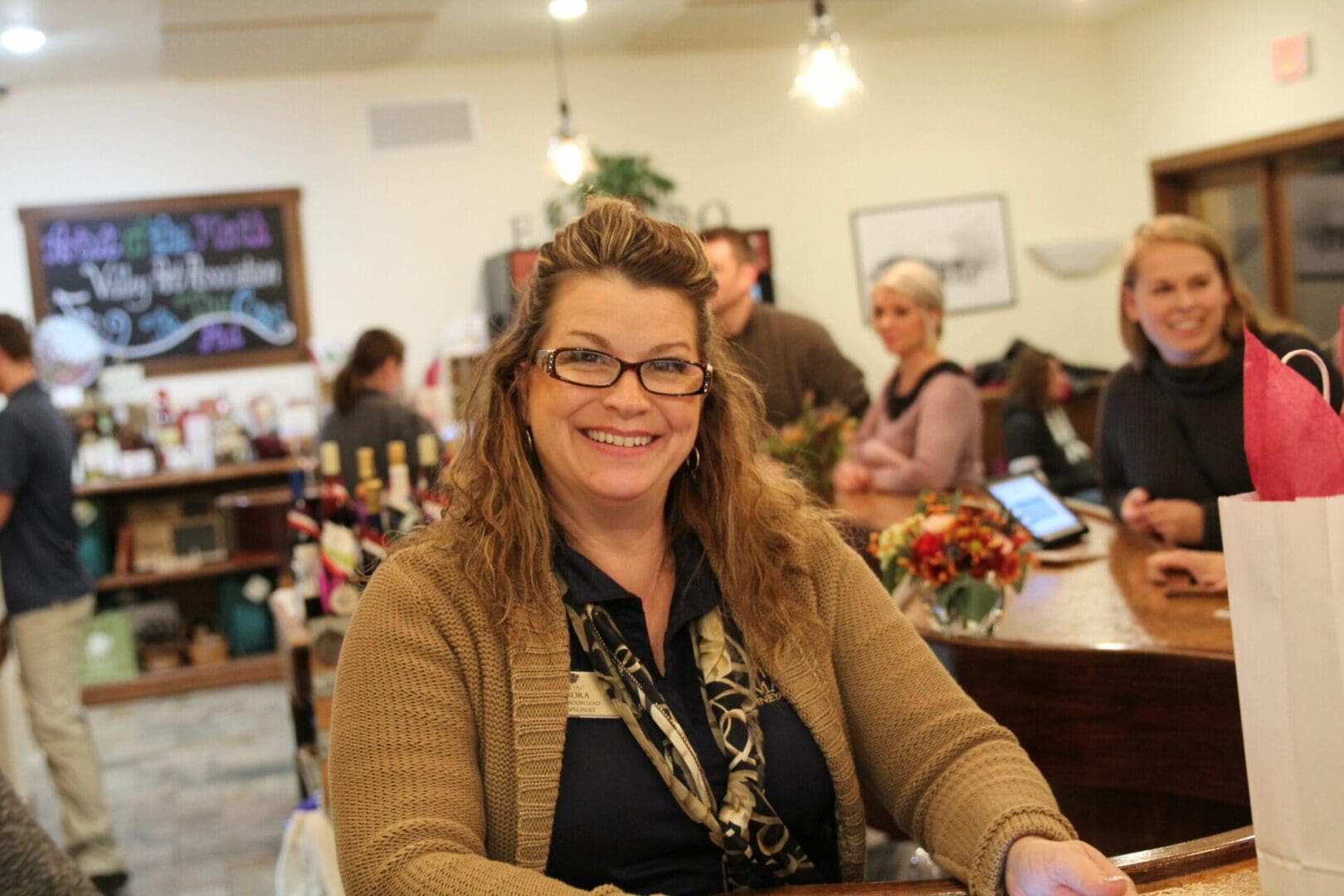 A woman smiles at the counter of a wine shop.