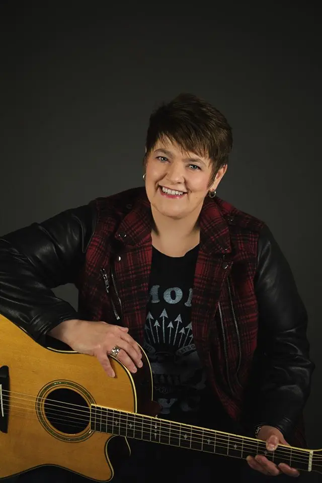 A woman smiling while holding an acoustic guitar.