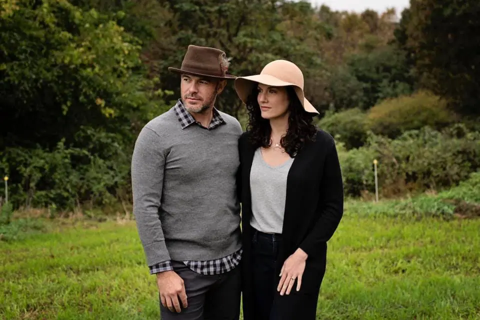 A man and woman standing in a field wearing hats.