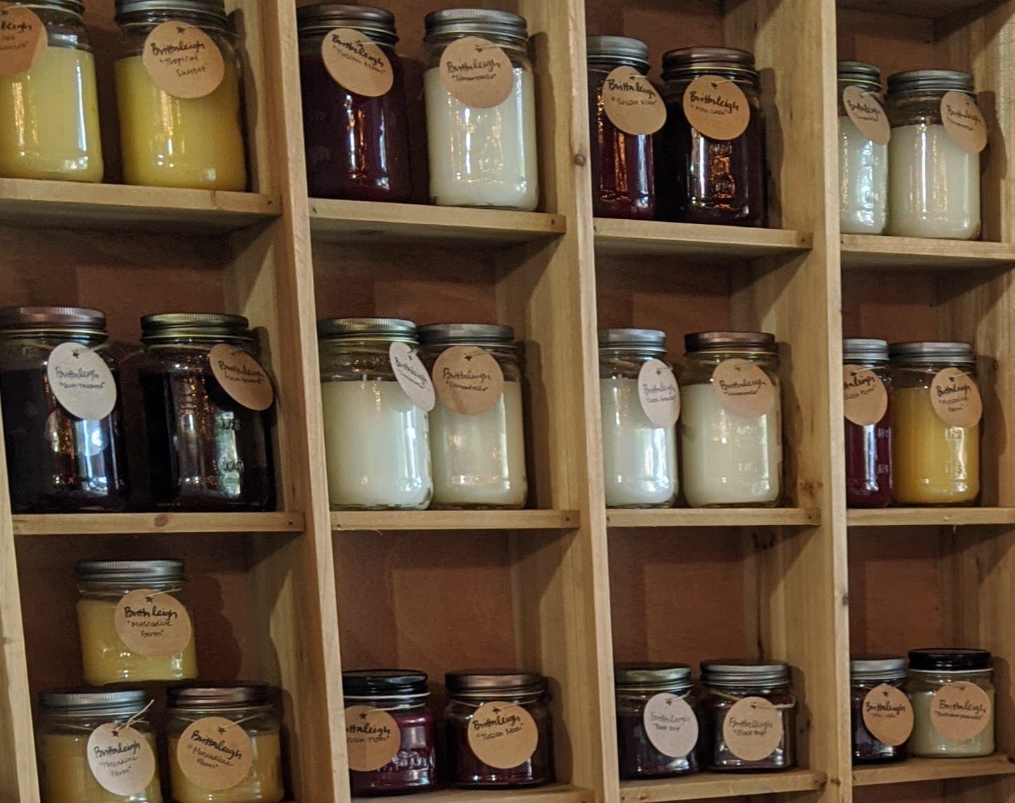 A wooden shelf with many jars of different kinds of jams and jellies.