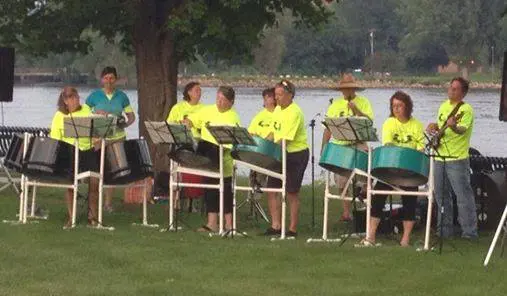 A group of people playing steel drums in front of a river.