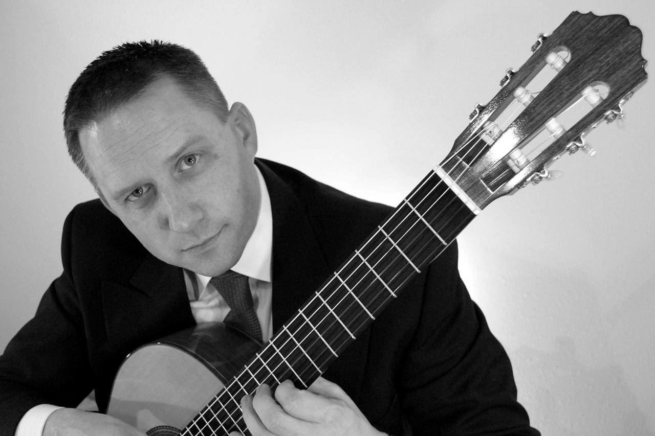 A black and white photo of a man playing an acoustic guitar.