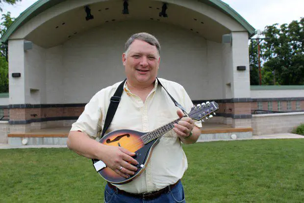 A man holding a mandolin in front of a building.