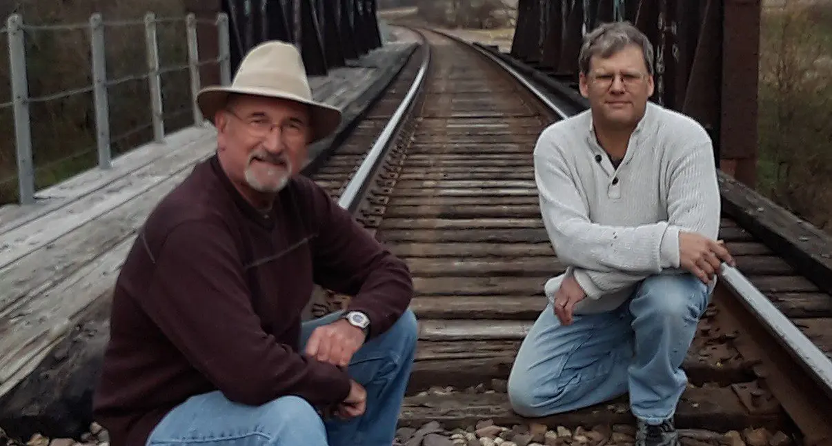 Two men crouching on a railroad track.