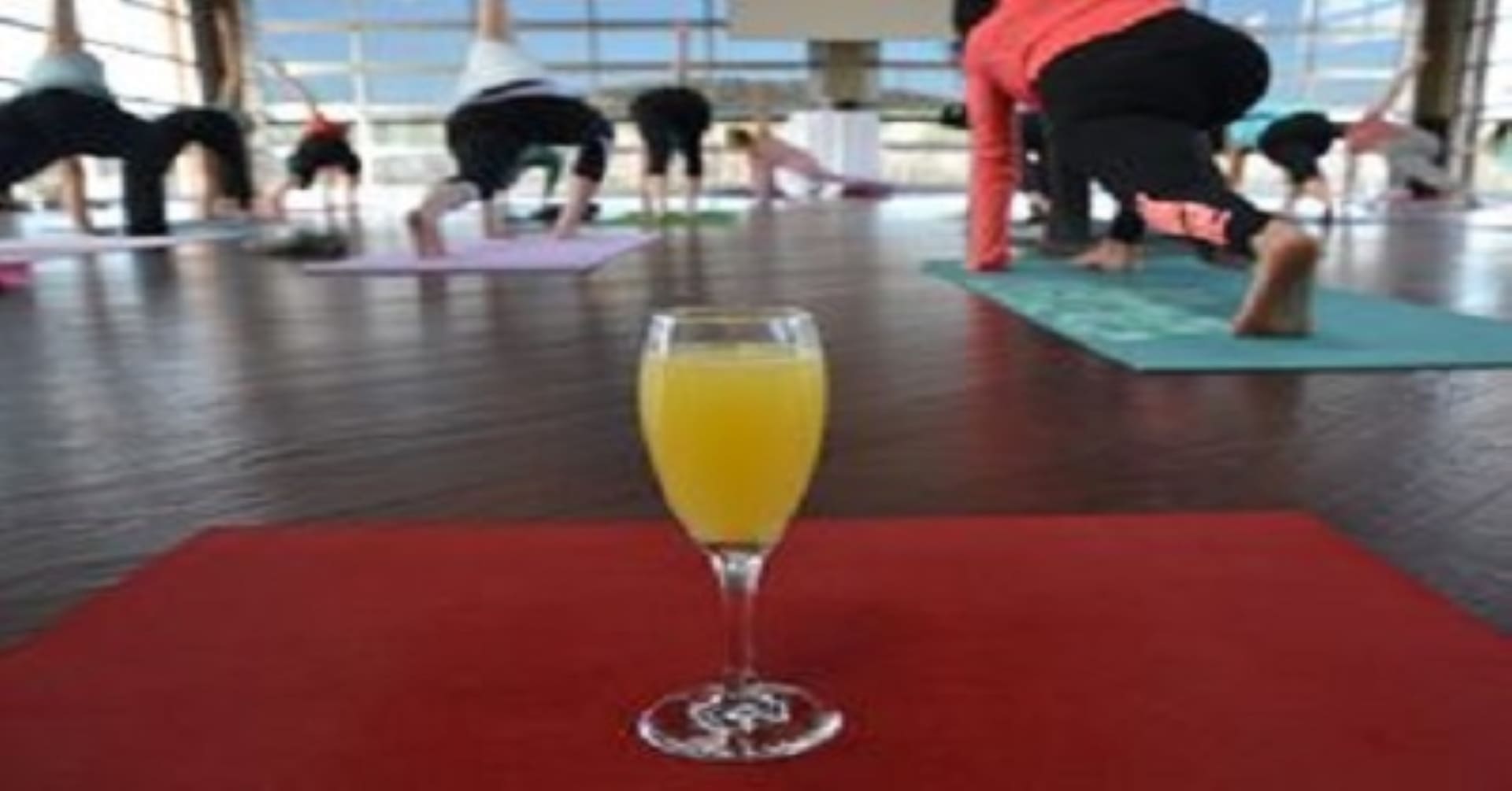 A glass of orange juice in front of a group of people doing yoga.