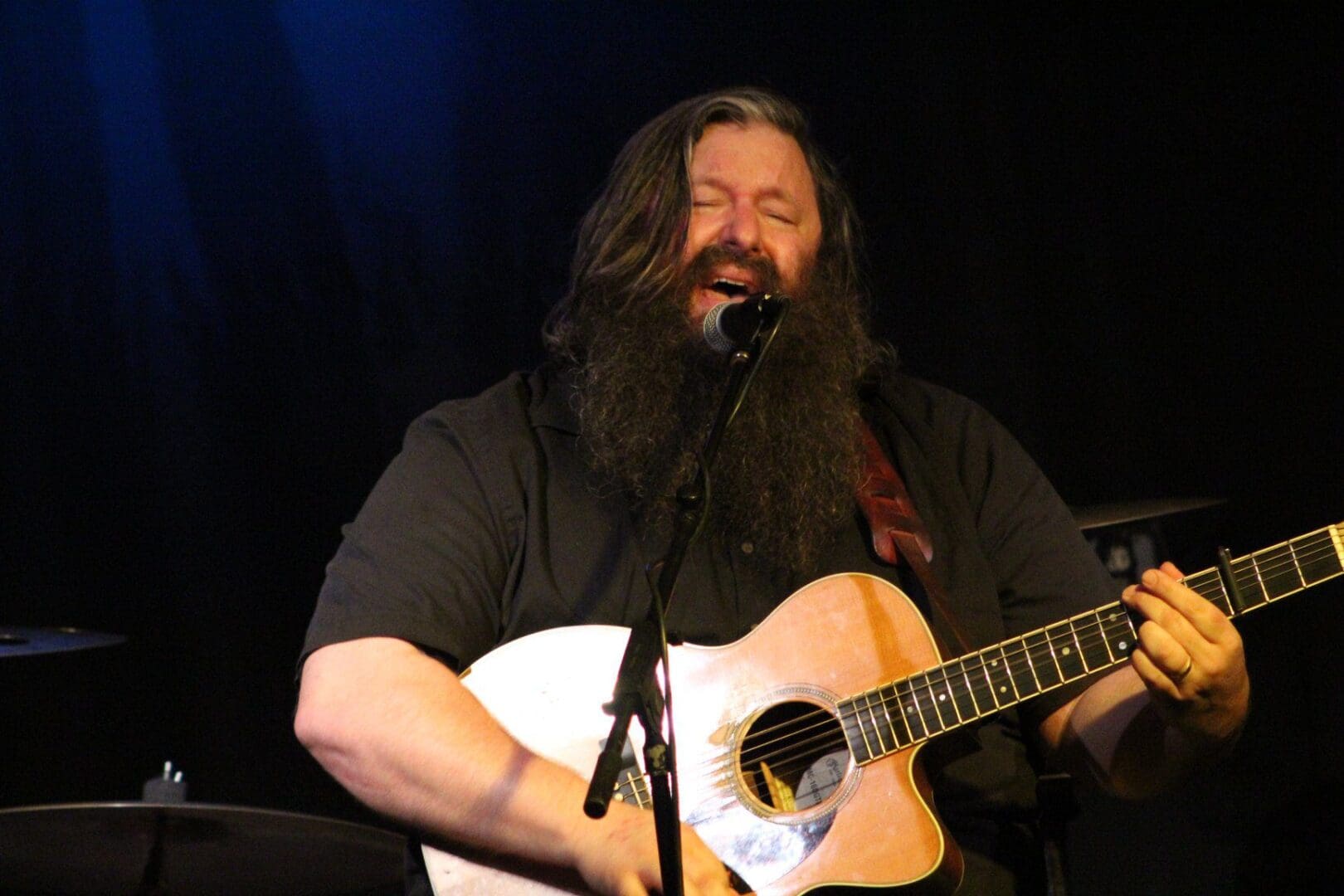 A man with a beard playing an acoustic guitar.