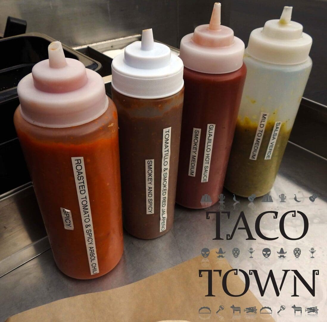 Four bottles of taco sauce are lined up on a counter.