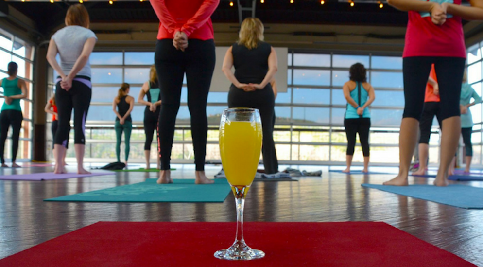 A glass of orange juice in front of a group of people in a yoga class.