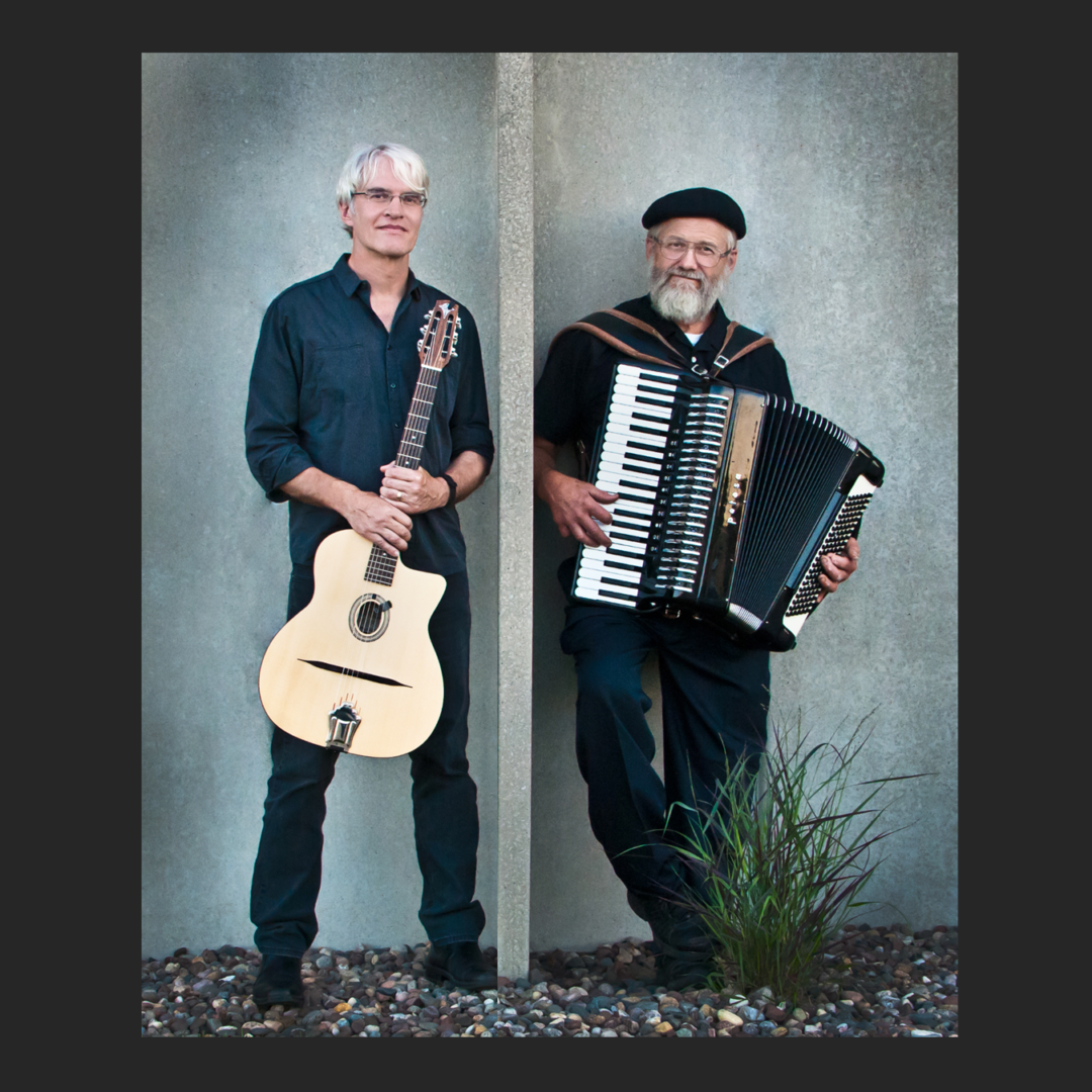 Two men standing next to each other holding an accordion.