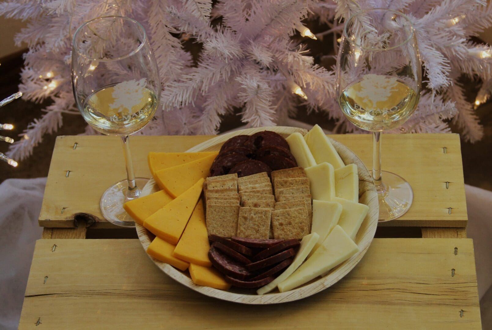 A plate of cheese, crackers, and wine glasses on a wooden crate.