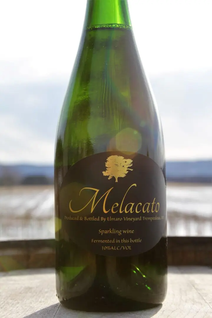 A bottle of melacata sits on a table in front of a field.