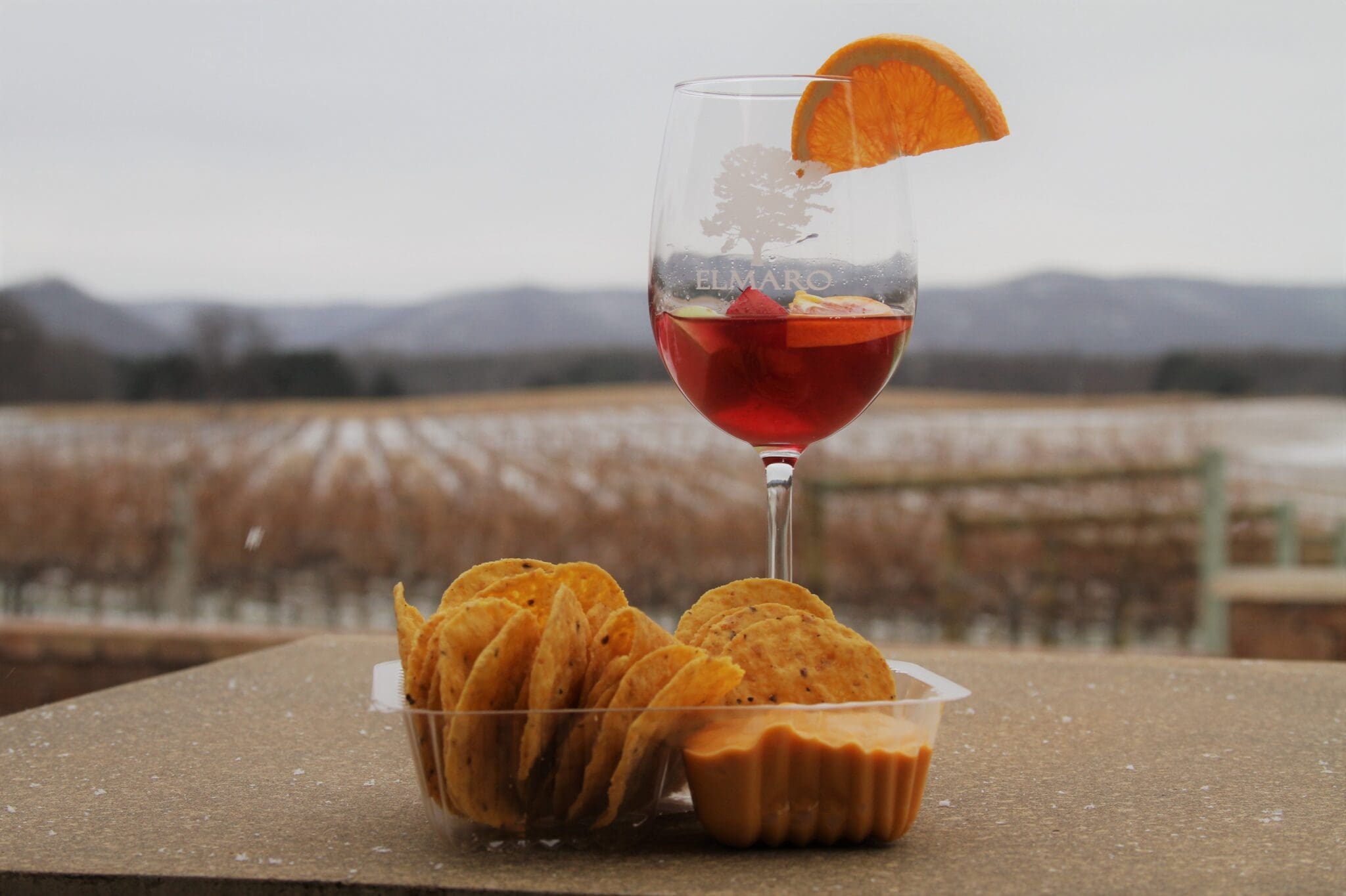 A glass of wine and chips on a table in front of a mountain.