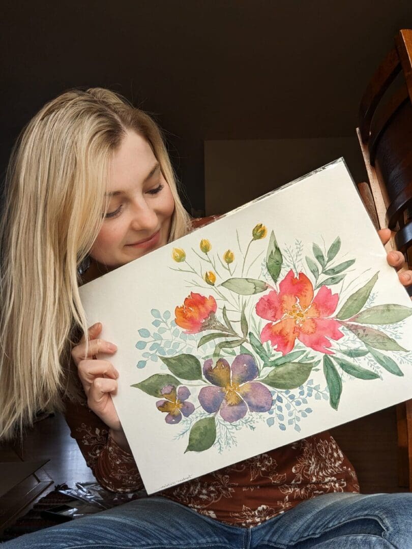 Woman holding a watercolor painting of flowers.