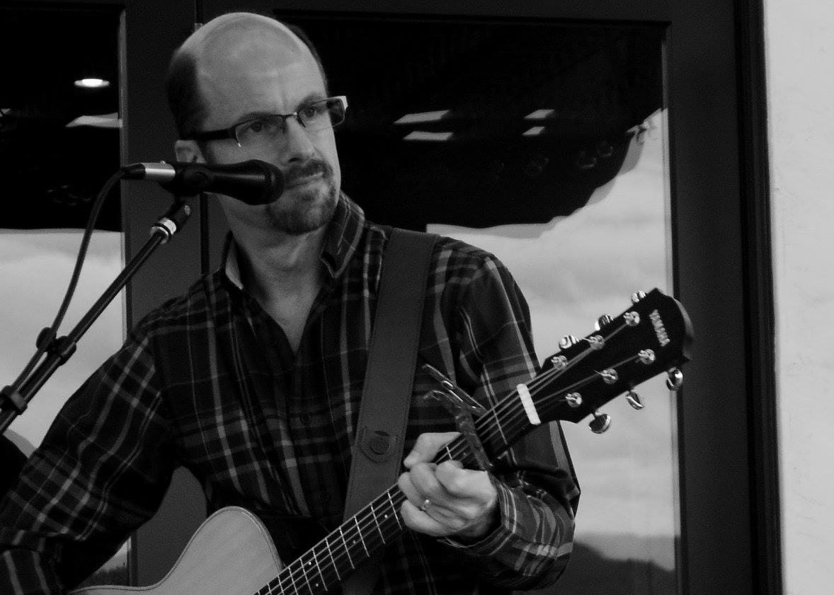 Man with glasses playing guitar on stage.