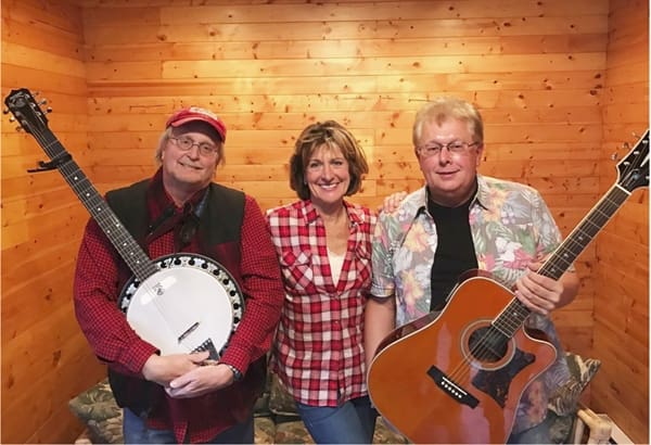 Three people smiling, two holding guitars, in a wooden room.