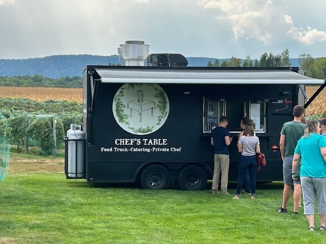 People ordering food at a black food truck named Chef's Table in a grassy outdoor area.