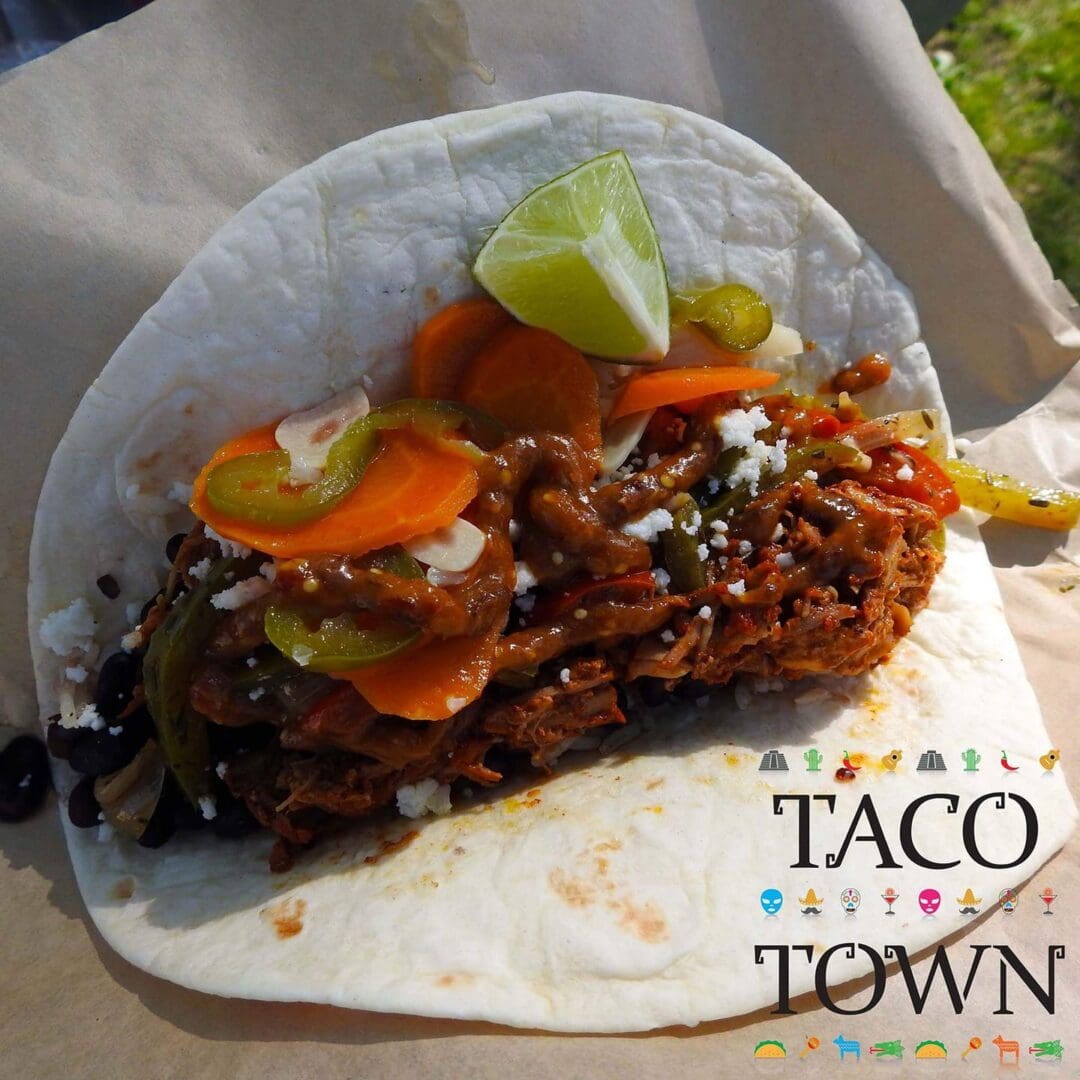 A delicious taco filled with meat, pickled vegetables, and a lime wedge.