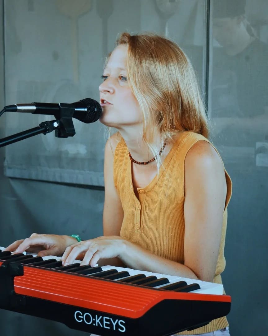 Woman singing and playing keyboard at a microphone.