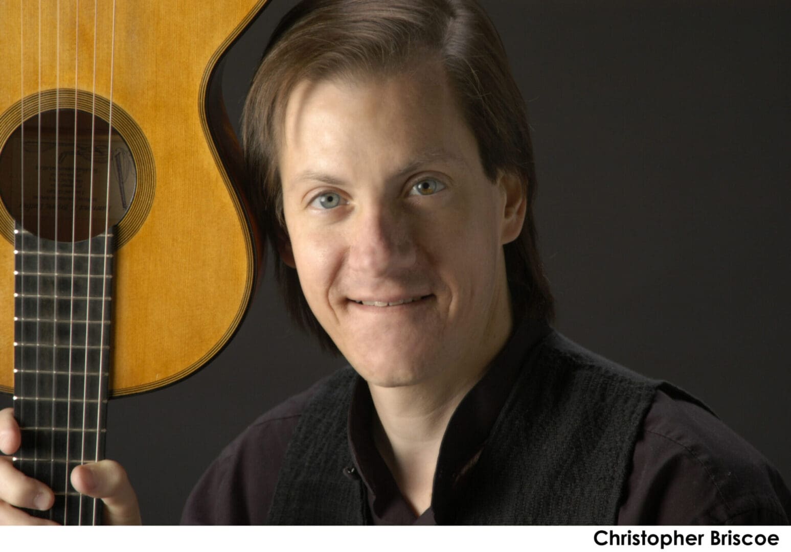 Man holding a guitar close to his face, smiling gently.