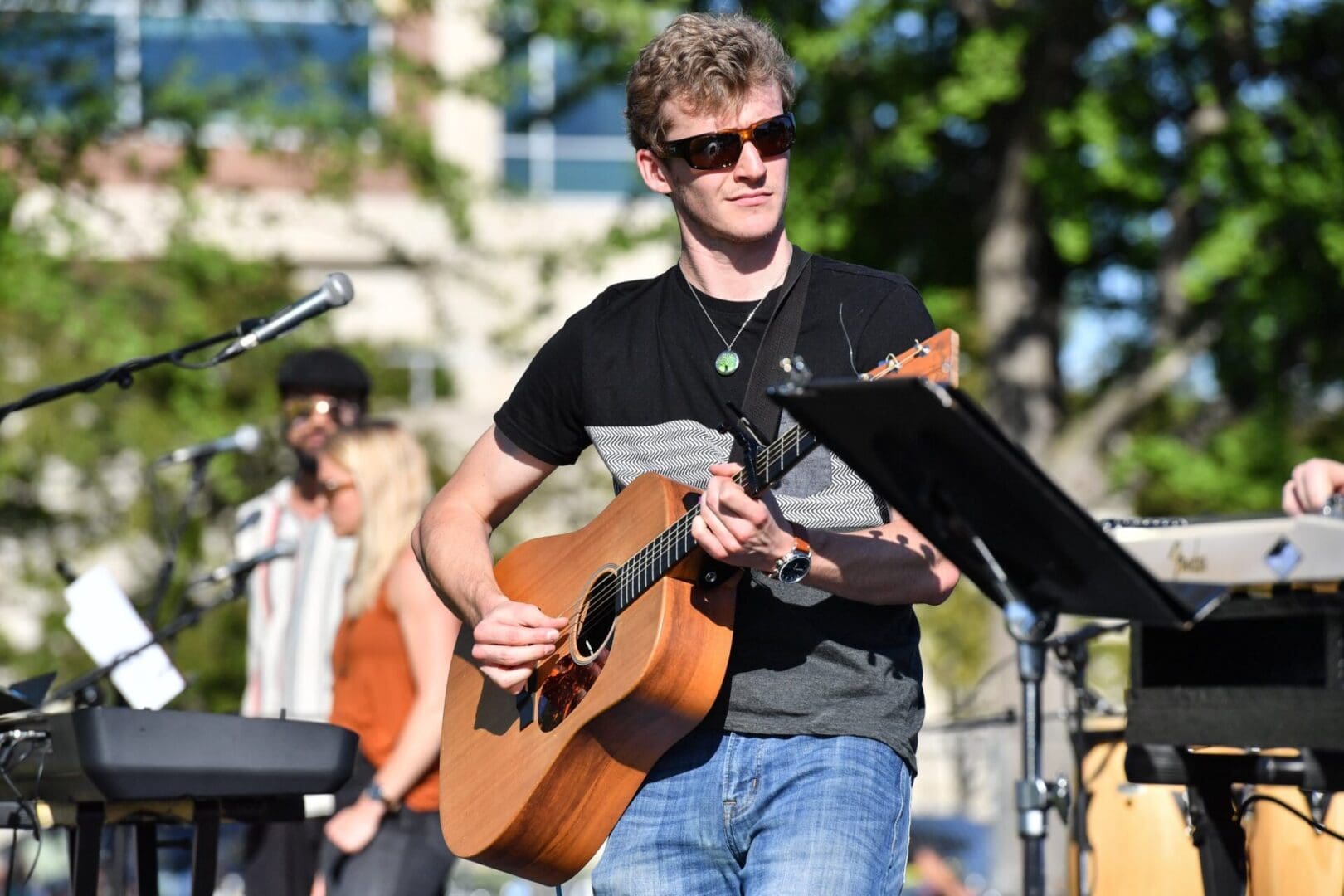 Man playing acoustic guitar outdoors during a live performance.