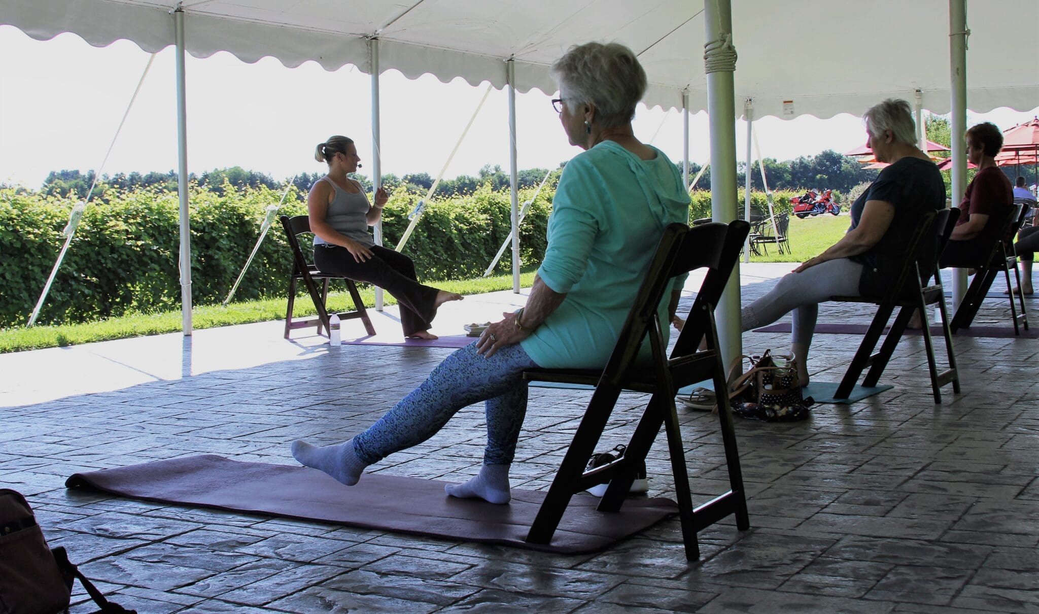 Group of women doing seated yoga exercises under a tent outdoors.