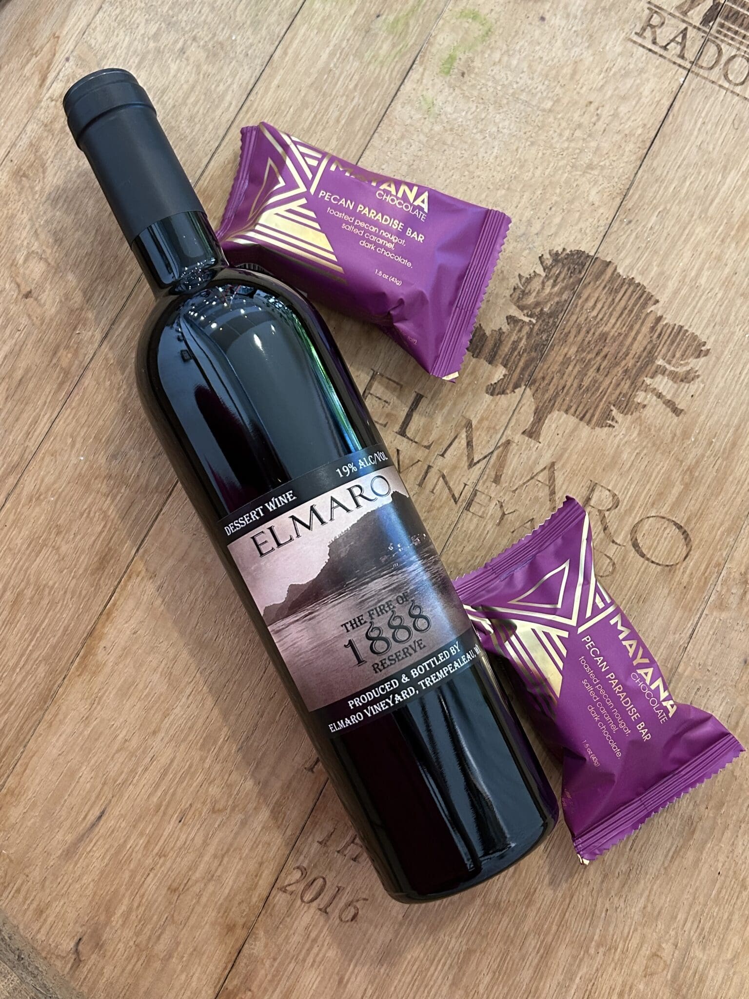 Bottle of Elmaro dessert wine with two Mayana chocolate bars on wooden surface.