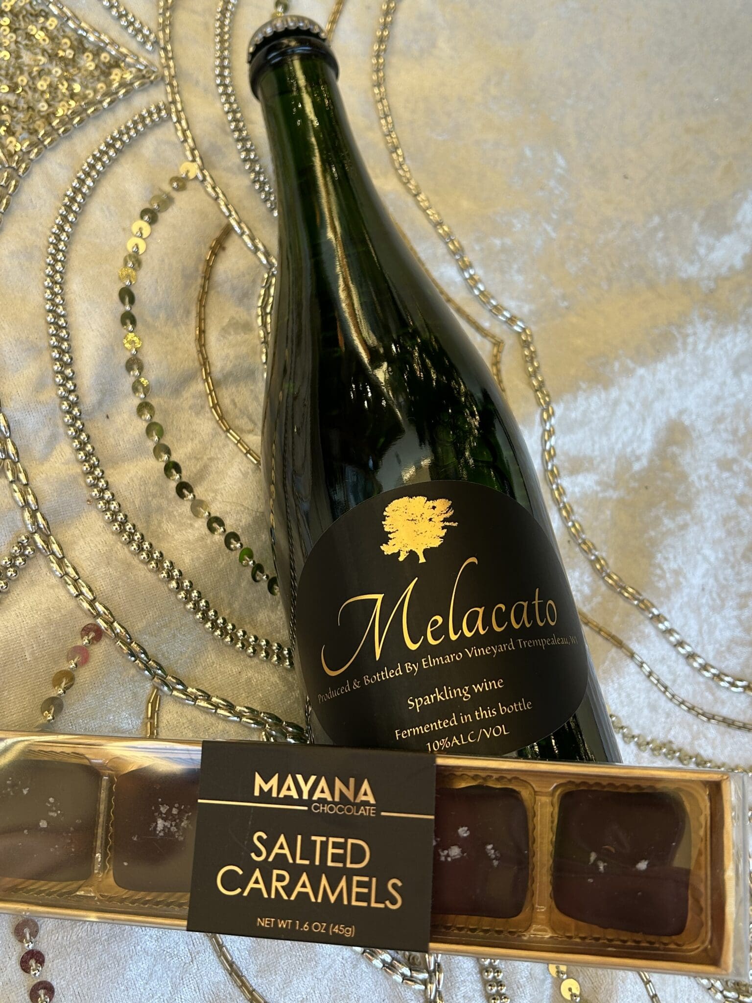 Bottle of Melacato sparkling wine with a box of Mayana salted caramels.